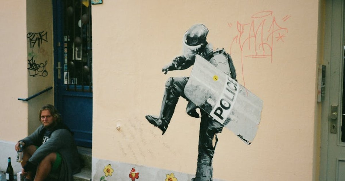 Street scene featuring graffiti art and a person sitting against a wall with bottles nearby.