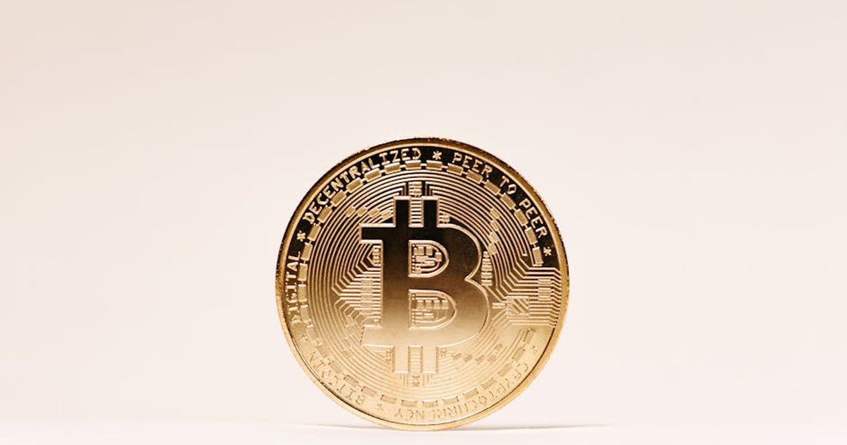 A golden Bitcoin coin standing upright against a minimalist light background.