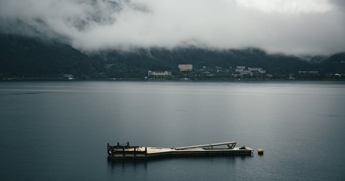 Tranquil view of Kawaguchiko Lake surrounded by misty mountains and a floating dock. Calm and peaceful setting.