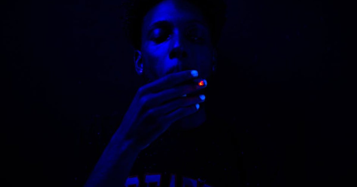 Close-up of a man smoking under blue ultraviolet lighting, creating a dramatic effect.