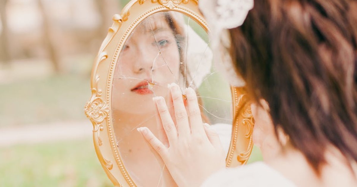 Artistic portrait of a woman looking into a cracked mirror outdoors in Hanoi, Vietnam.