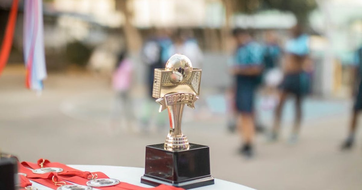 Close-up of a polished soccer trophy with medals at an outdoor sports award ceremony.