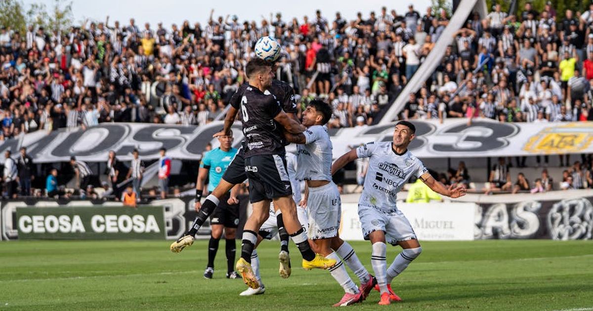 Soccer players in action during a competitive match with a lively crowd in the background.