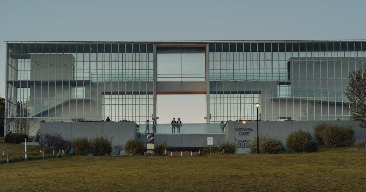 Sleek modern glass building facade in Tokyo at dusk with small group of people.