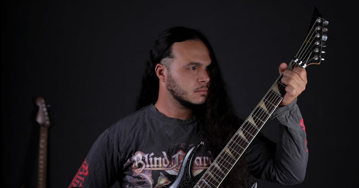 Musician with long hair playing electric guitar on stage in dark setting.