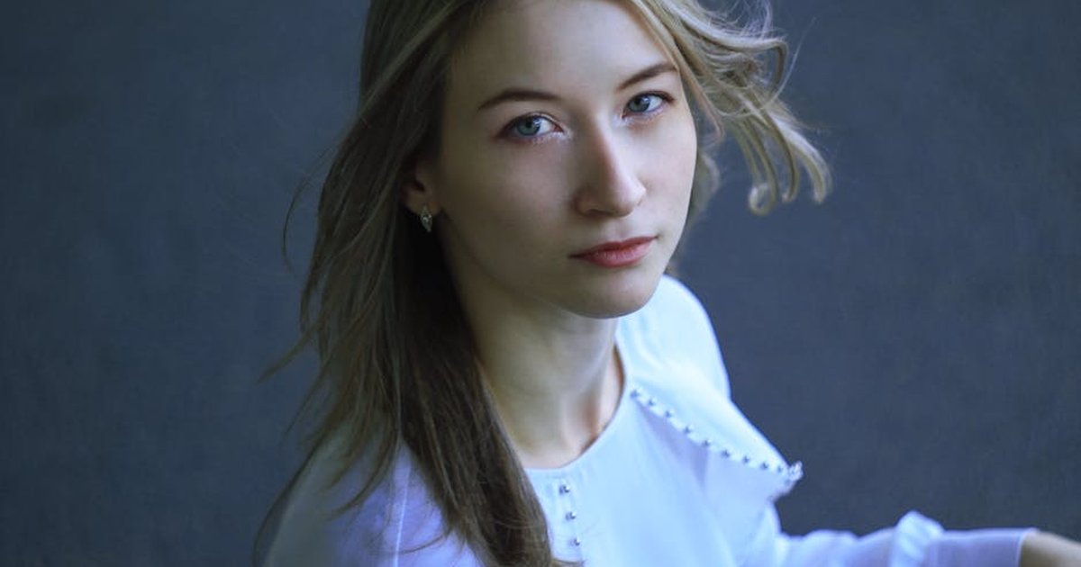 Portrait of a blonde woman looking upwards with soft lighting and a neutral background, creating an elegant mood.