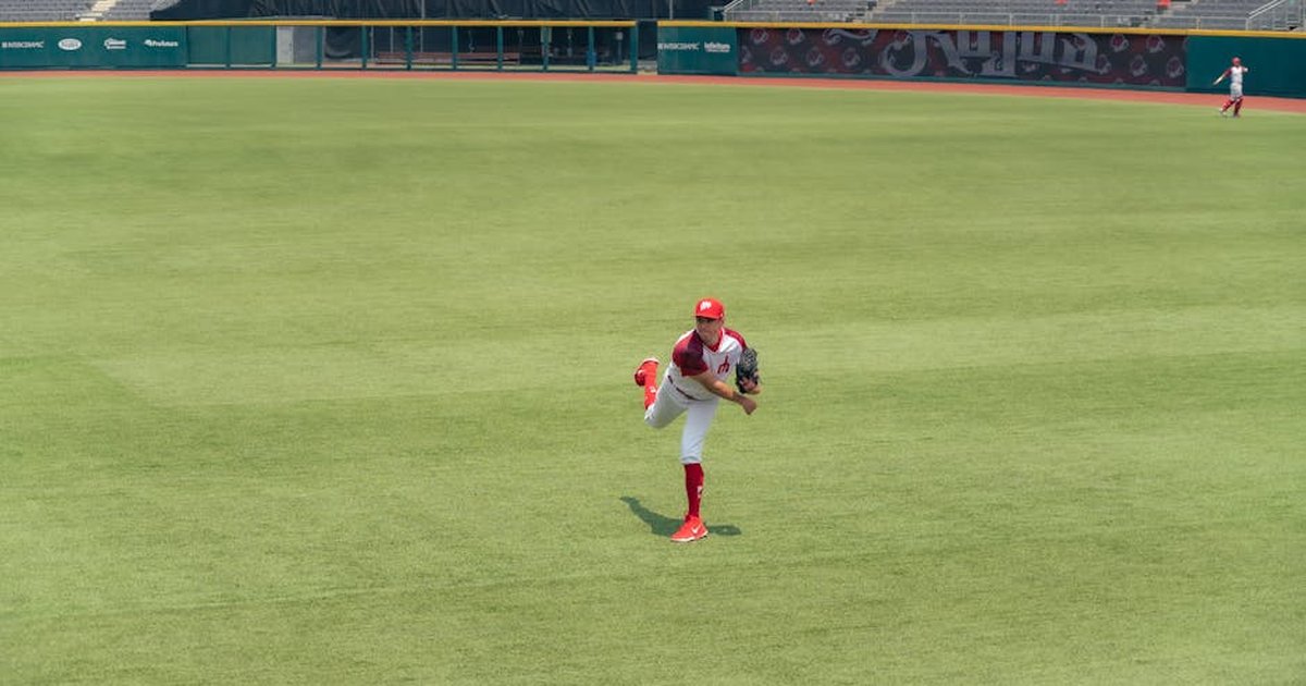 A baseball player pitching on a grass field in an empty stadium.