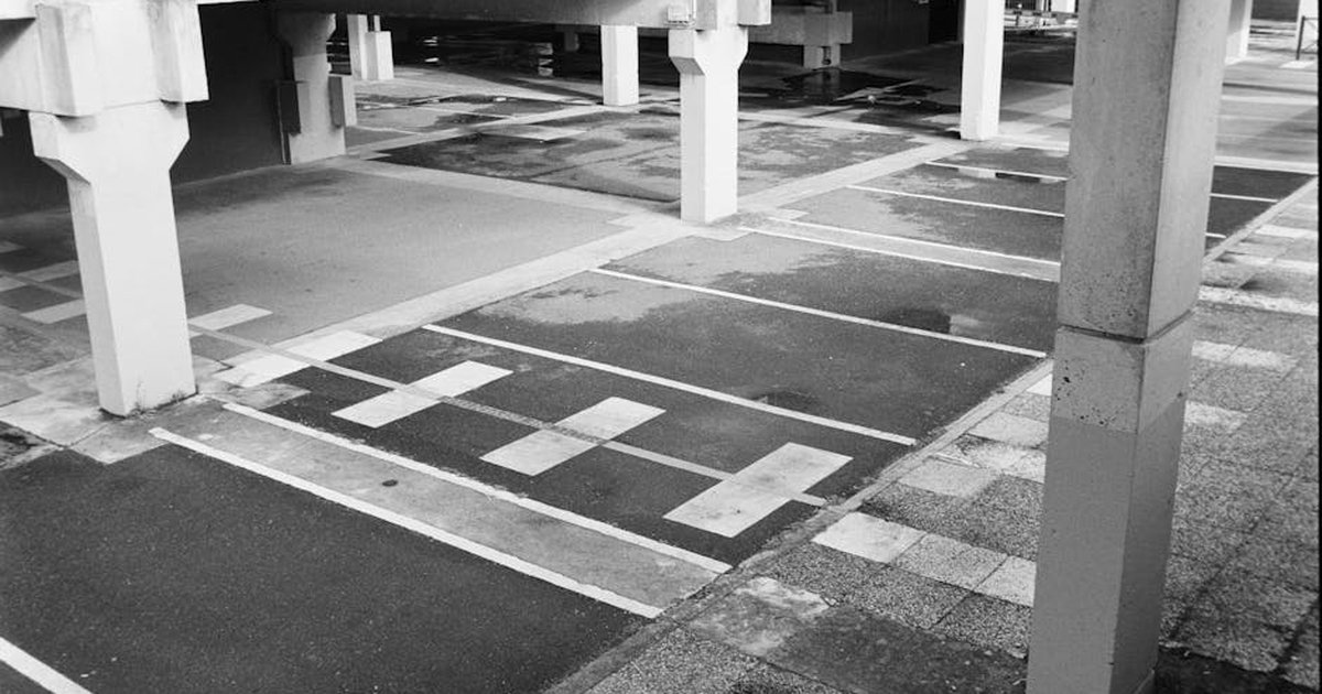 Black and white image of an empty urban parking lot with concrete pillars, offering a minimalist architectural scene.
