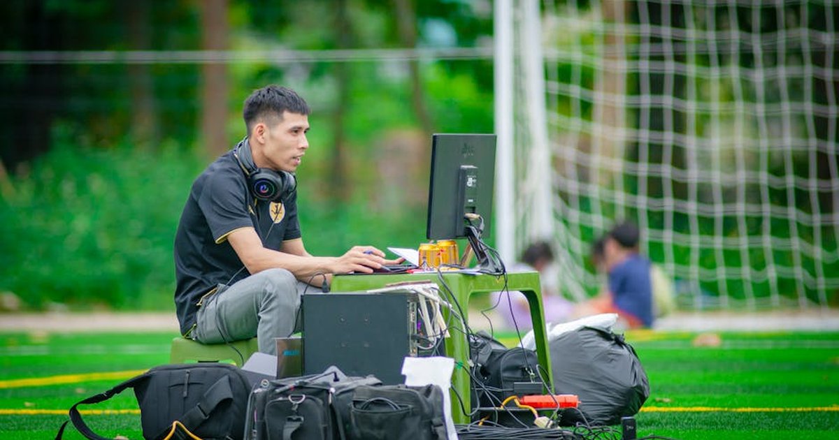 Man working at a computer setup on a football field in Hanoi, Vietnam.