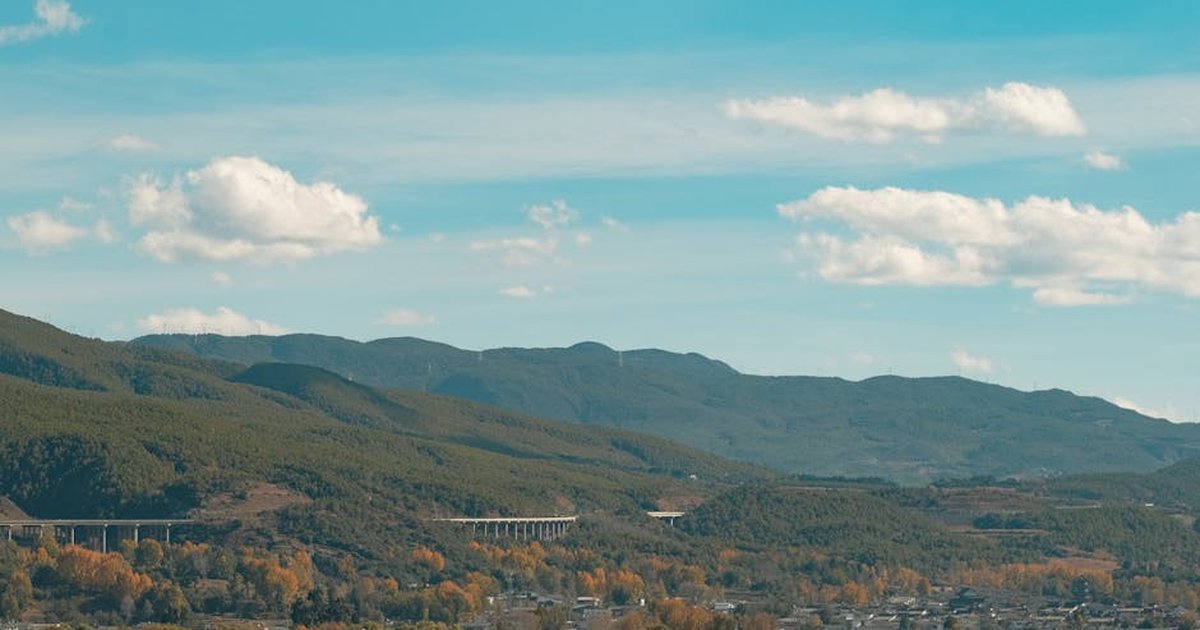 A picturesque landscape of Dali mountains with a viaduct and autumn foliage under a blue sky.