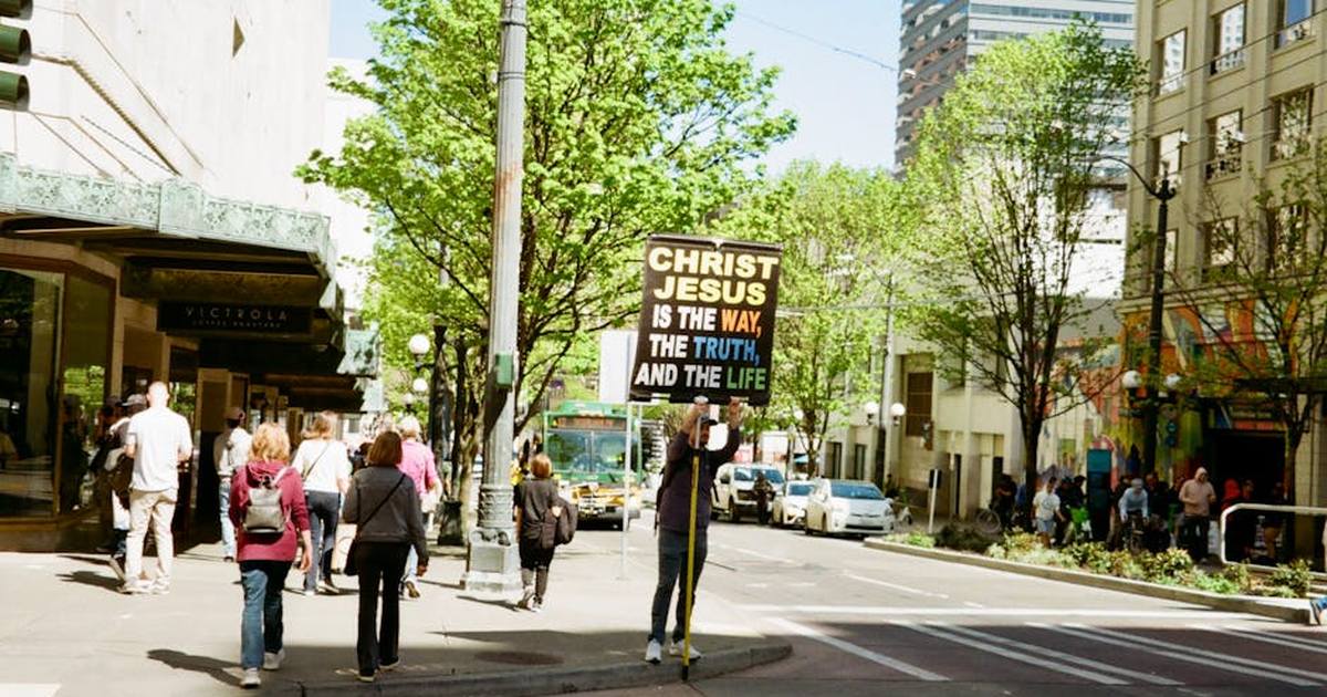 Urban scene with a person holding a sign about Christ Jesus in bright daylight.