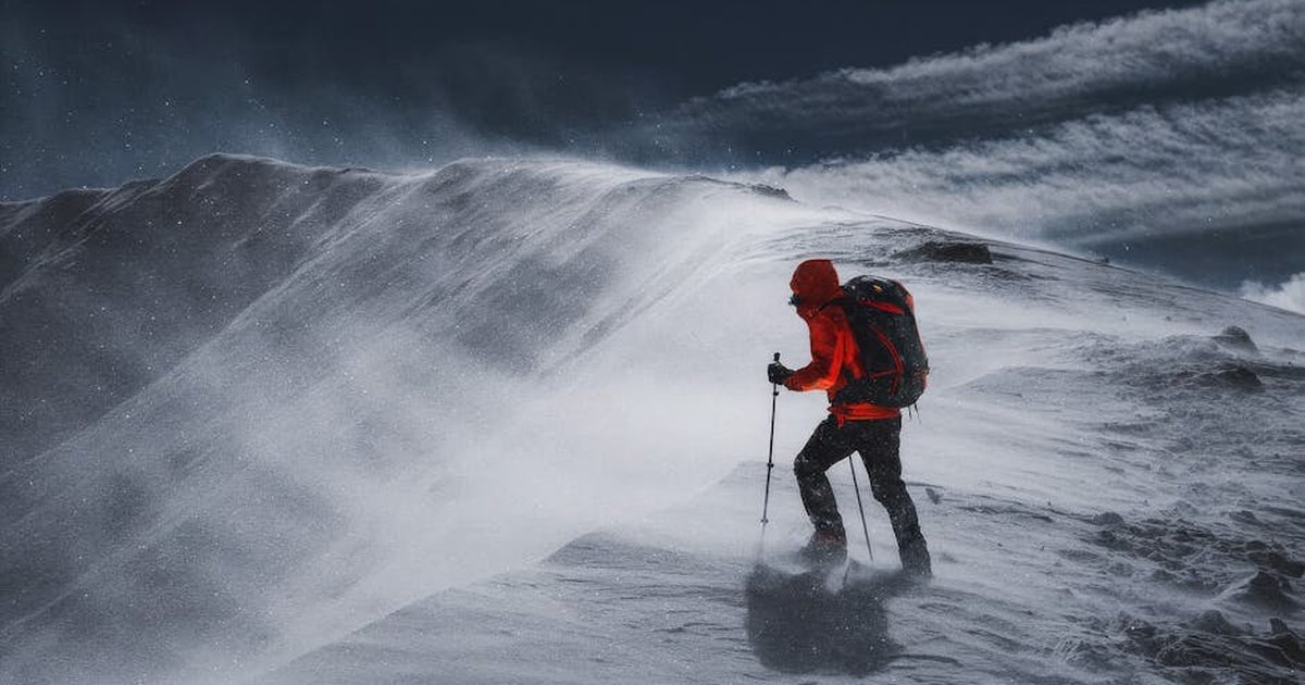 A determined hiker battles through a snowy mountain ridge during a harsh winter storm.