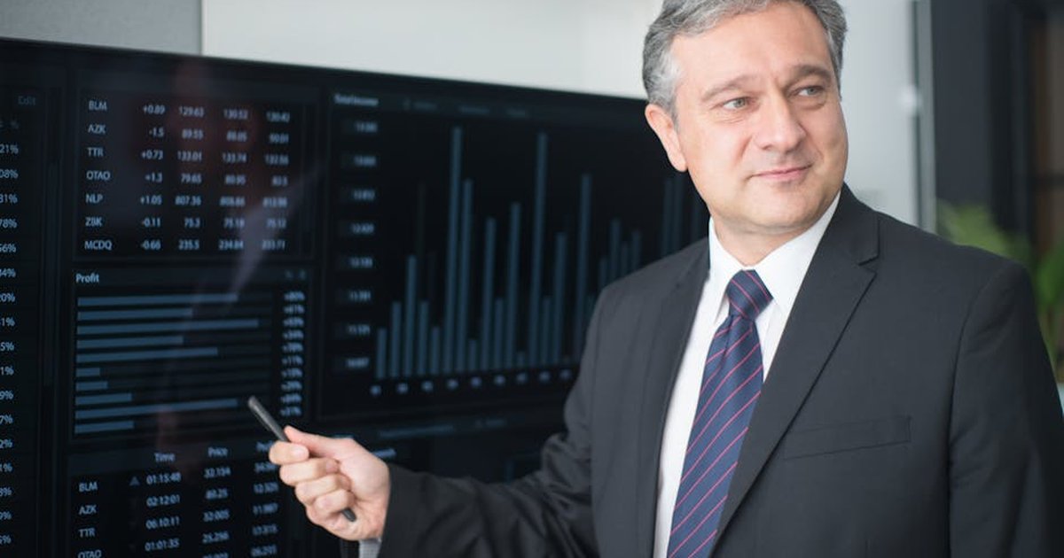 Professional man in suit reviewing financial charts on monitor, showcasing stock market trends.