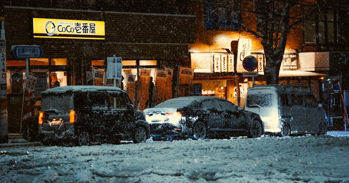 Snow-covered cars outside a lit Tokyo restaurant at night, capturing winter's beauty.