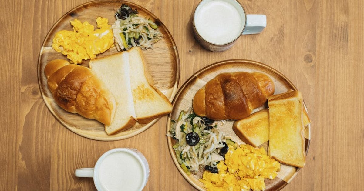 Delicious Japanese breakfast featuring eggs, toast, and milk on a wooden table setting.