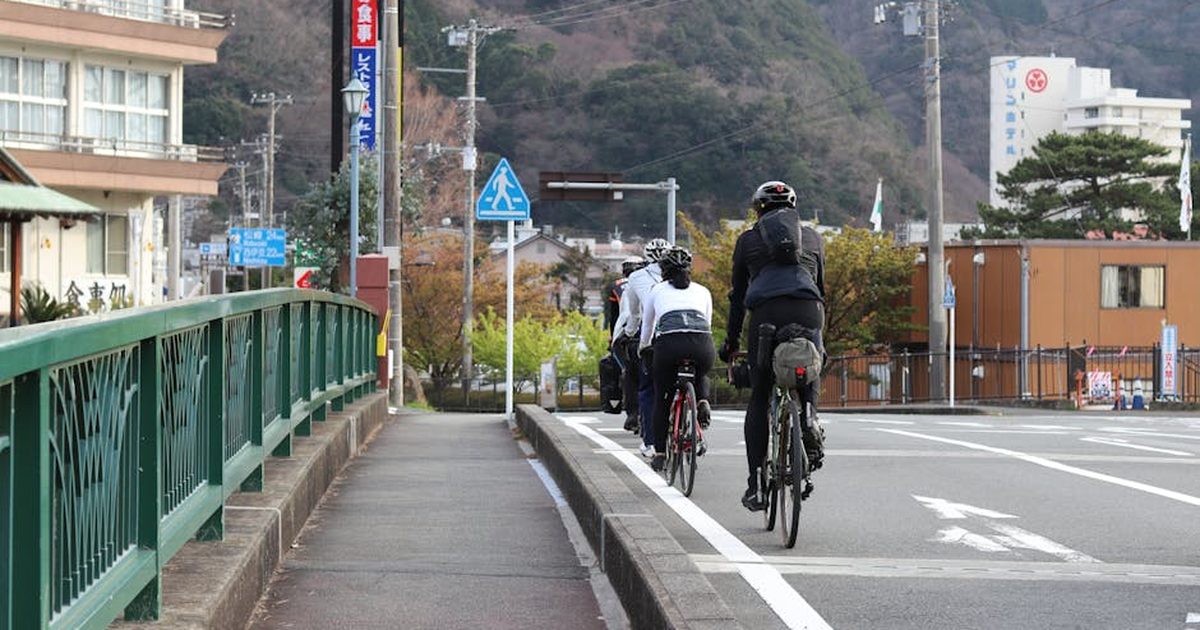 Group of cyclists riding through the streets of Itō, Shizuoka, Japan, with scenic mountain backdrop.