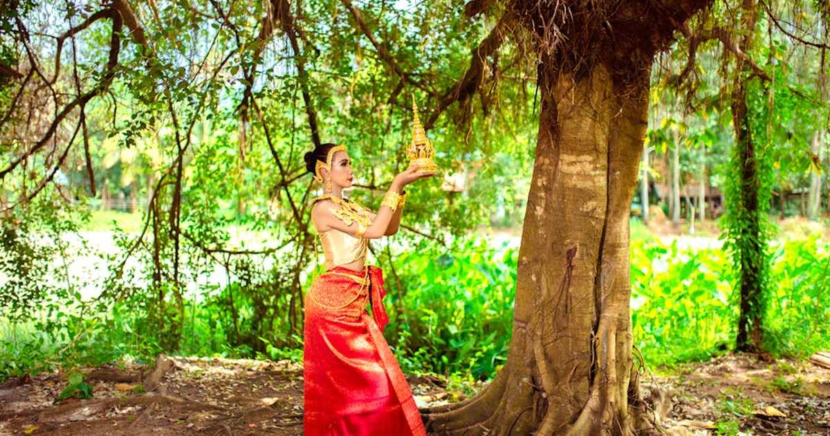 A woman in traditional Cambodian attire poses in a park holding a golden headdress.