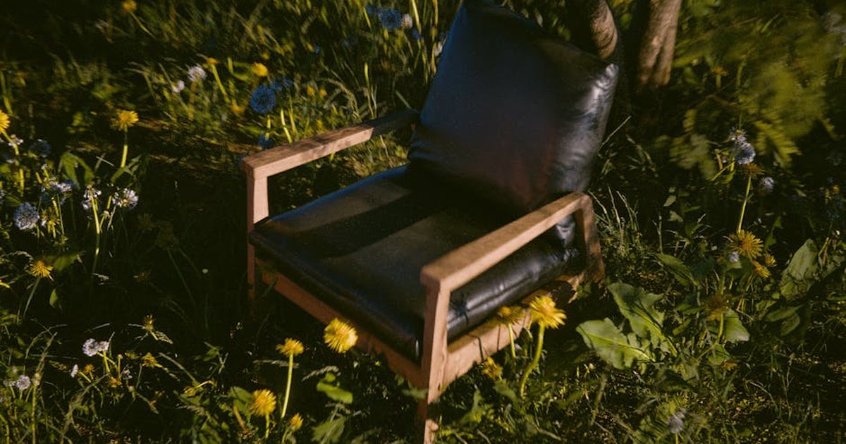 Cozy black chair on wooden frame amidst blooming meadow flowers, offering a serene outdoor retreat.