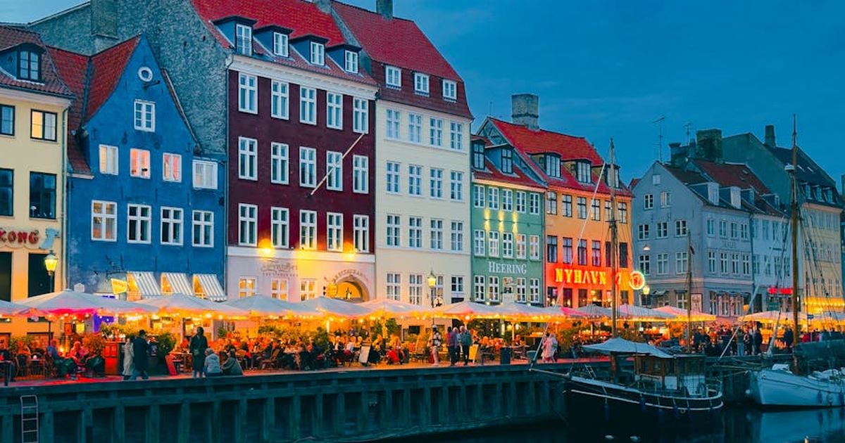 Vibrant buildings and waterfront cafes line the Nyhavn Canal in Copenhagen, Denmark, at dusk.