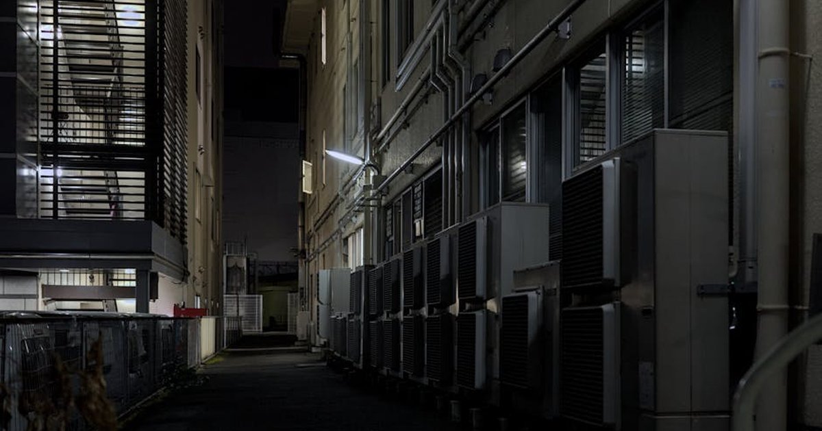 A dimly lit urban alley in Kyoto featuring air conditioning units, captured at night.