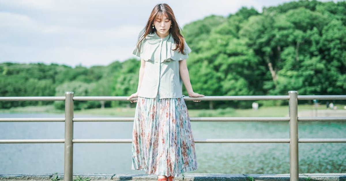 Elegant woman in floral dress standing beside a serene lake during a sunny day.