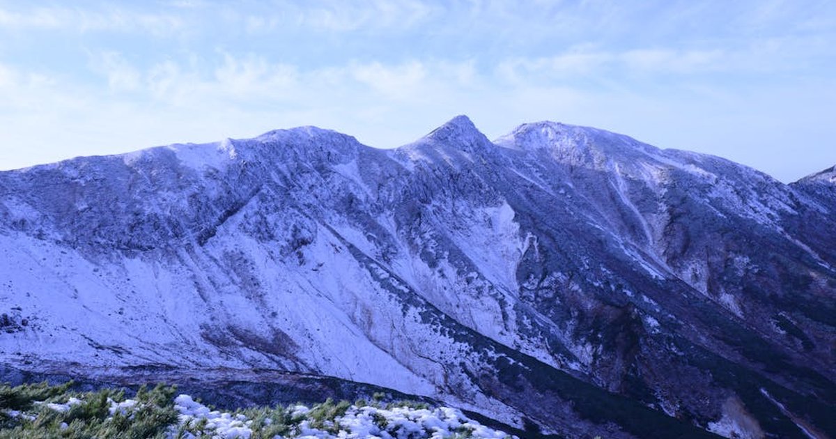 Breathtaking view of snowcapped mountains in Hokkaido, Japan with grass and shrubs in the foreground.