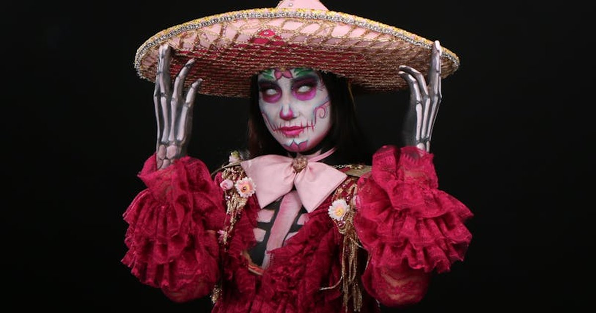 Person dressed in vibrant Day of the Dead attire with detailed face paint, emphasizing Mexican traditions.