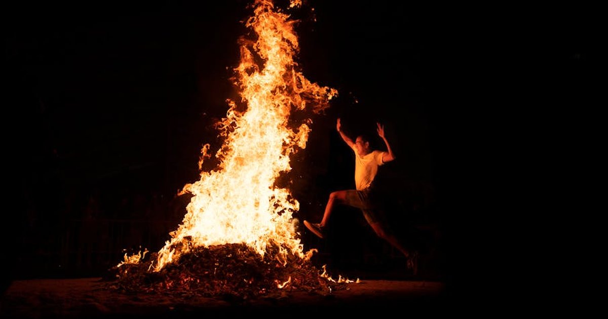 An adventurous man leaps over a large bonfire during a night celebration, highlighting energy and tradition.