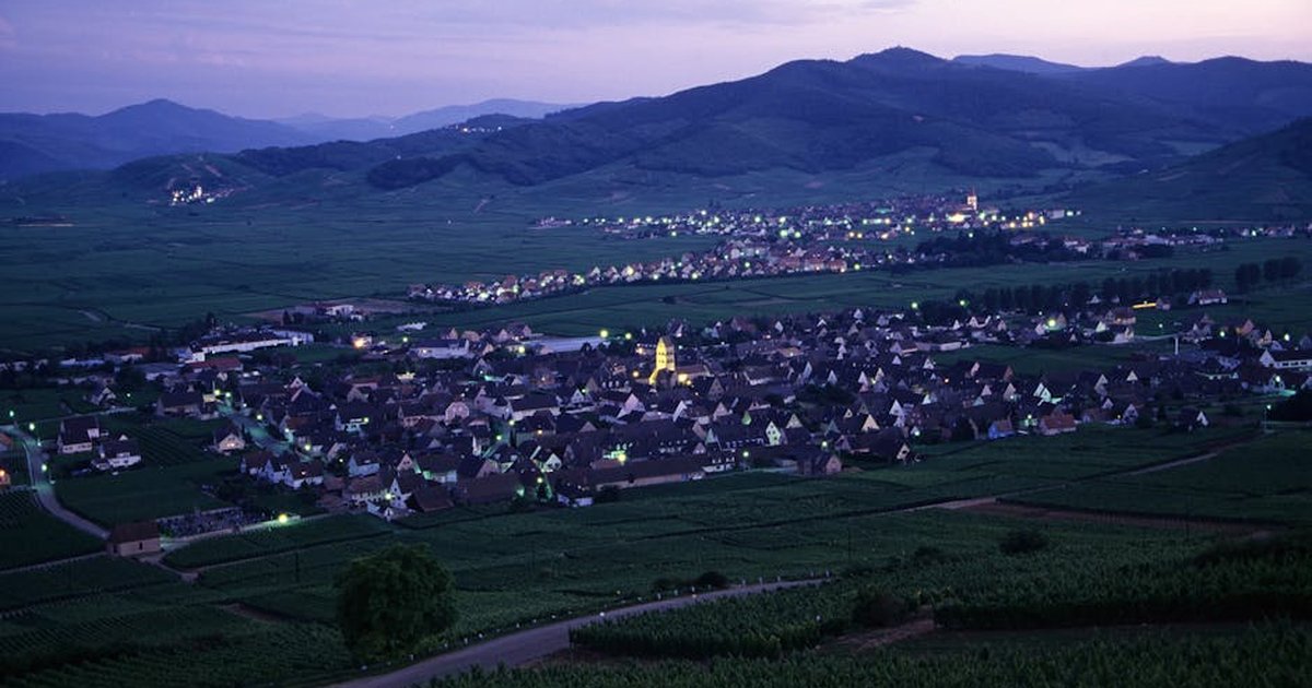 A charming hillside village in Alsace surrounded by vineyards at twilight, with mountain views.