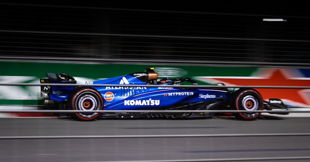 Blue Formula car speeding on track during night race.