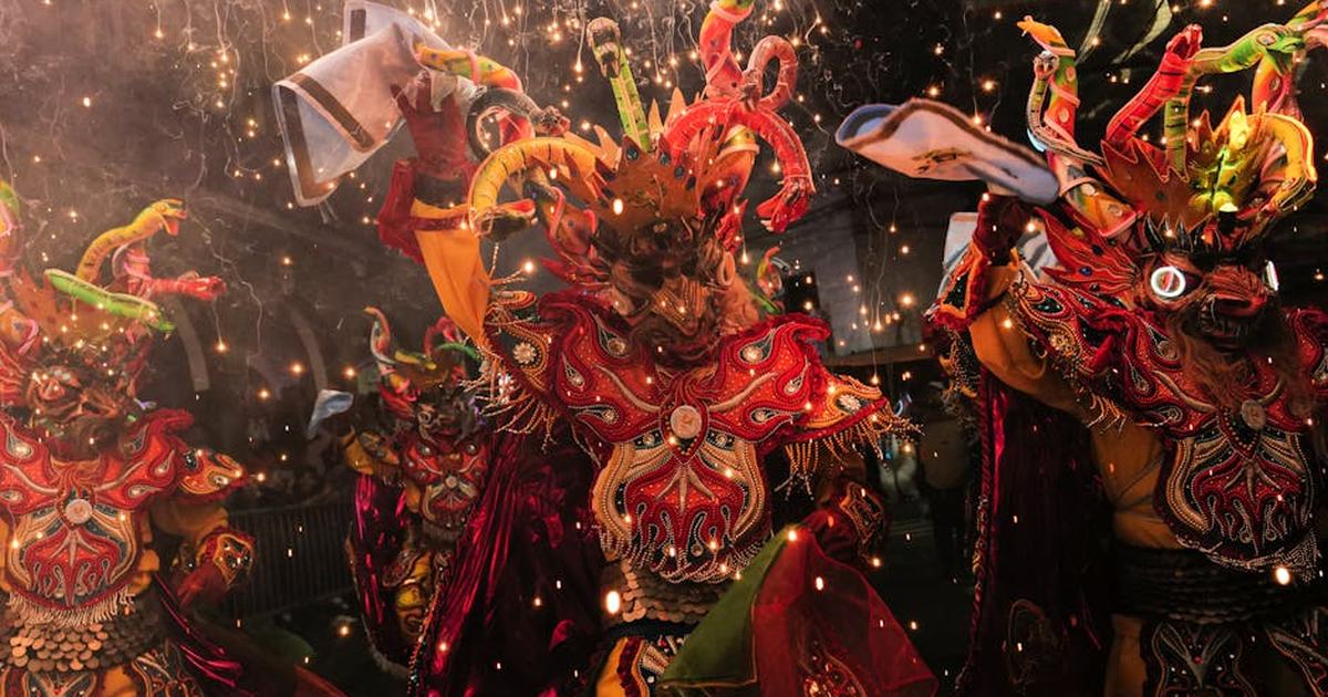 Colorful Bolivian carnival dancers in traditional costumes with sparklers and fireworks at night.