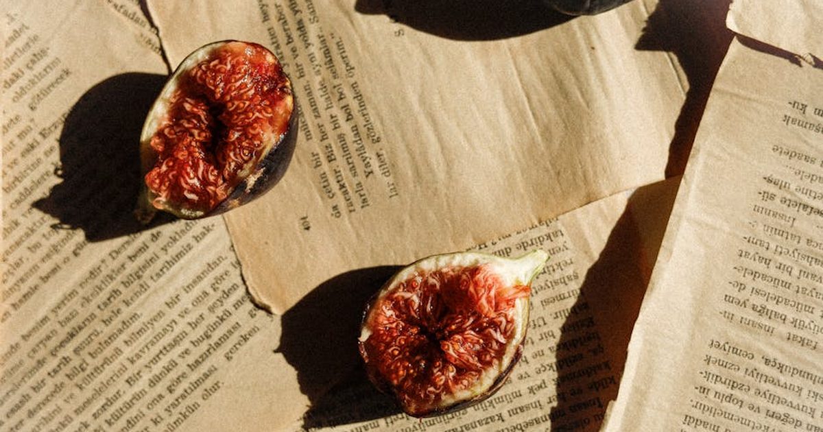 Sunlit figs rest on vintage book pages, casting artistic shadows. Perfect for culinary or vintage themes.