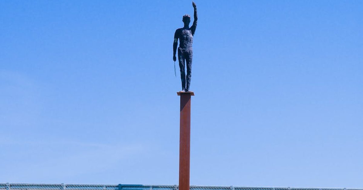 A striking statue of a figure with a flag stands prominently against a clear blue sky.