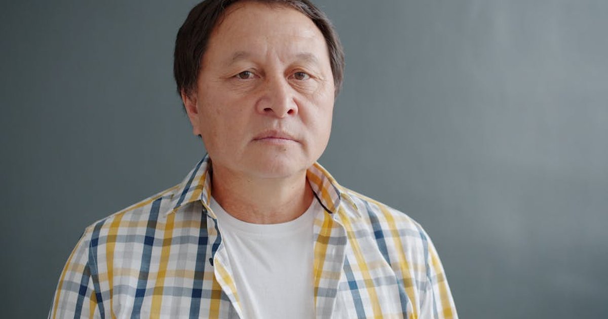 Close-up portrait of a man wearing a plaid shirt against a gray background.