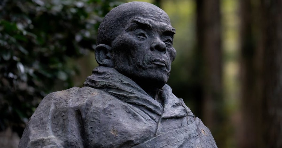 A close-up of a historic Japanese monk statue situated in a tranquil forest setting, capturing cultural essence.