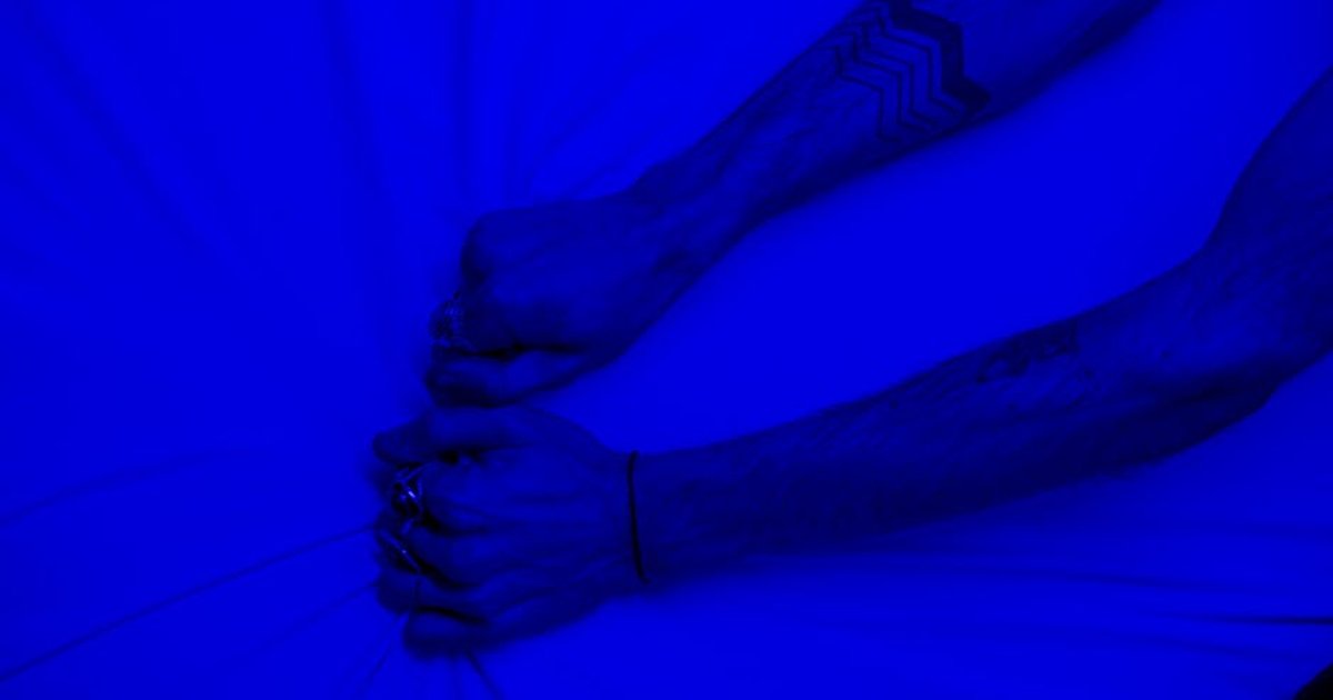Close-up of tattooed arms pulling fabric under intense blue lighting, symbolizing stress or frustration.