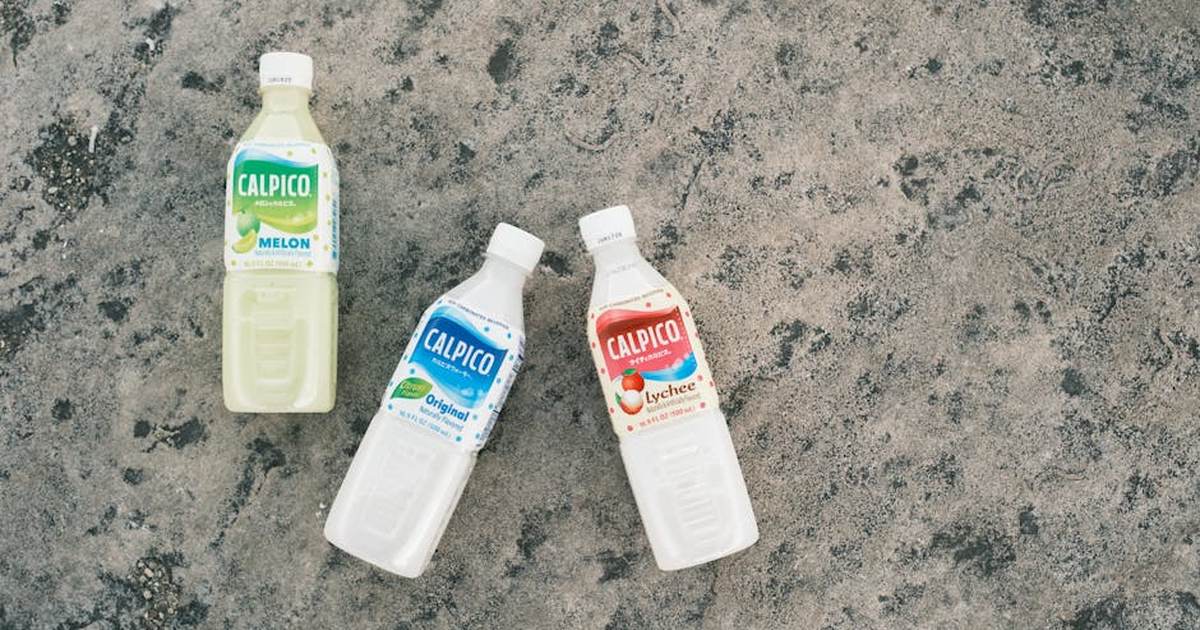 Three Calpico drink bottles in different flavors on a textured concrete background.