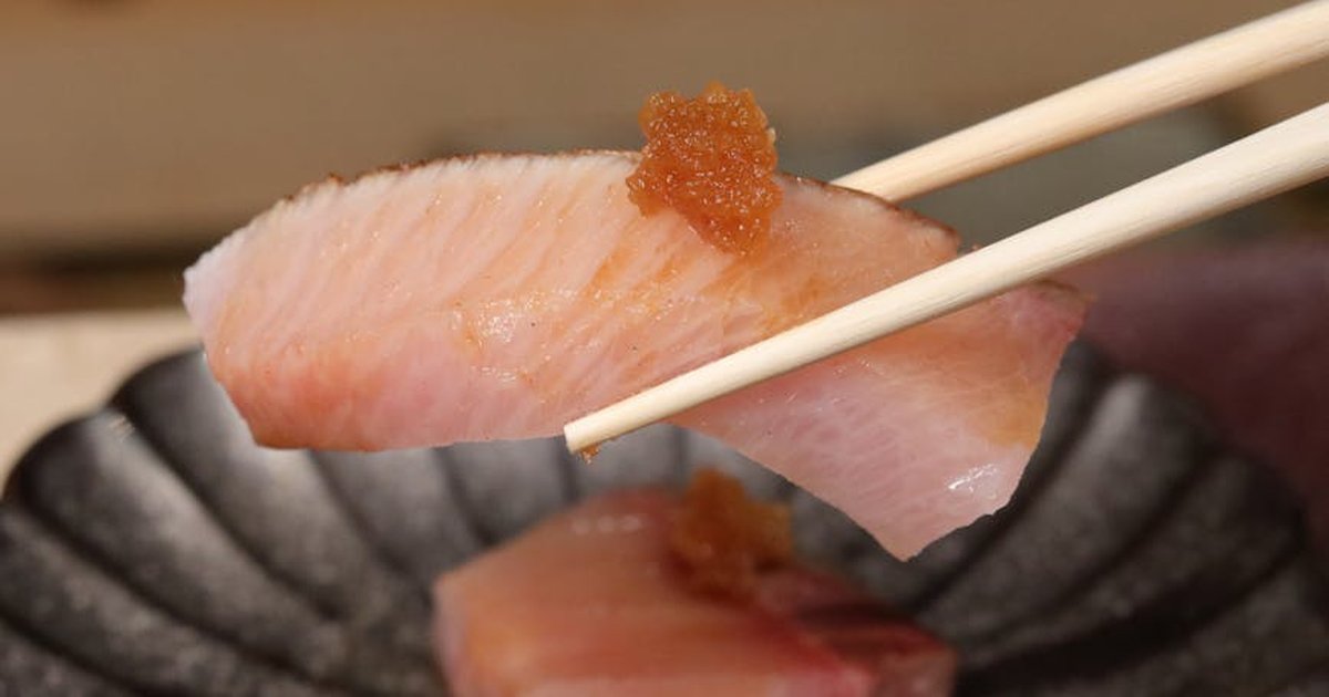 Delicious sashimi piece held by chopsticks, garnished with roe, on a black plate.