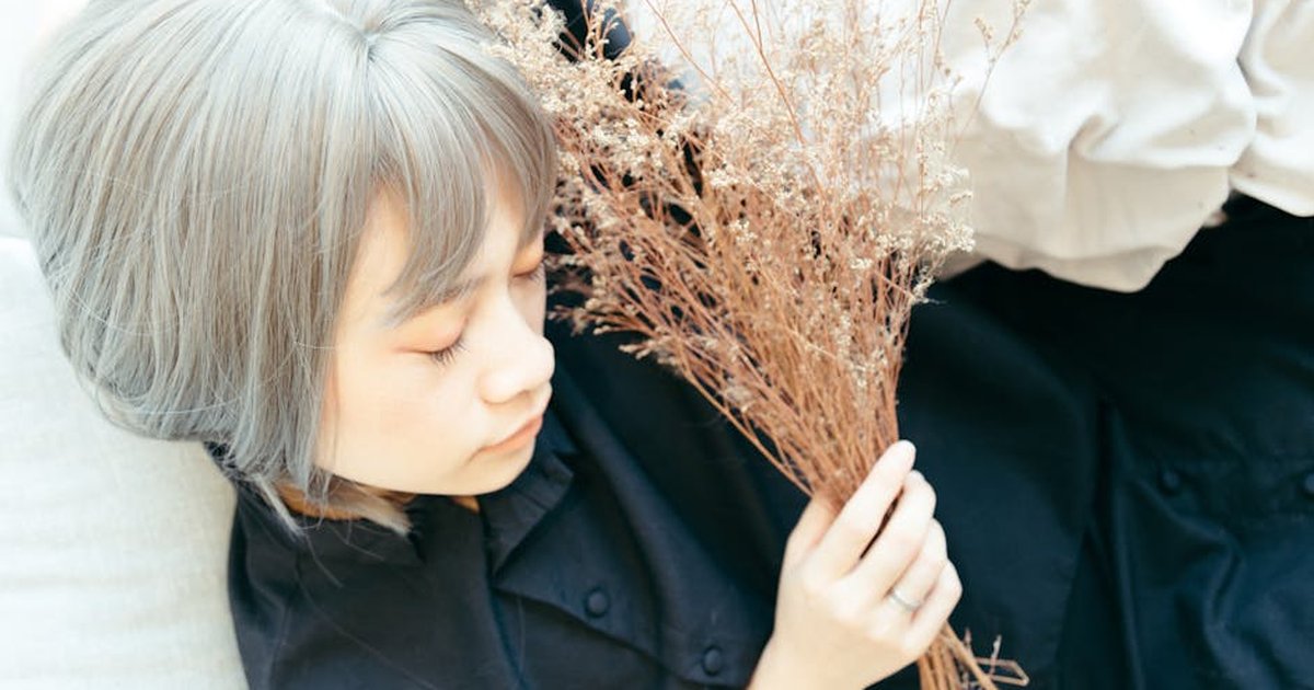 A serene woman with gray hair in a black dress holding dried flowers, eyes closed.