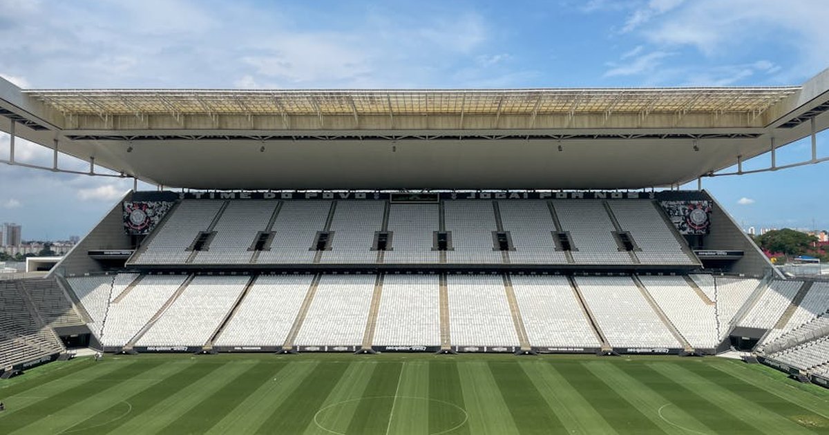 Wide view of an empty football arena in São Paulo, featuring a green pitch under a sunny sky.