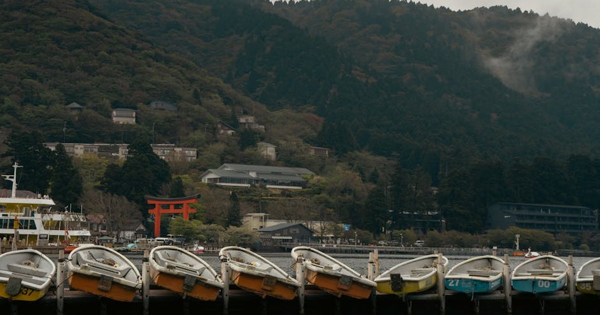 Serene waterfront view with boats and iconic Torii gate against lush mountains in Hakone, Japan.