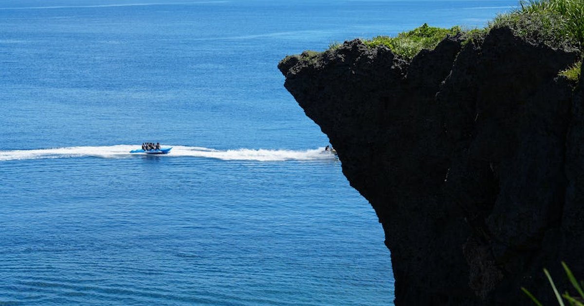 A vivid ocean scene with a kayak gliding by a rugged cliff edge under bright daylight.