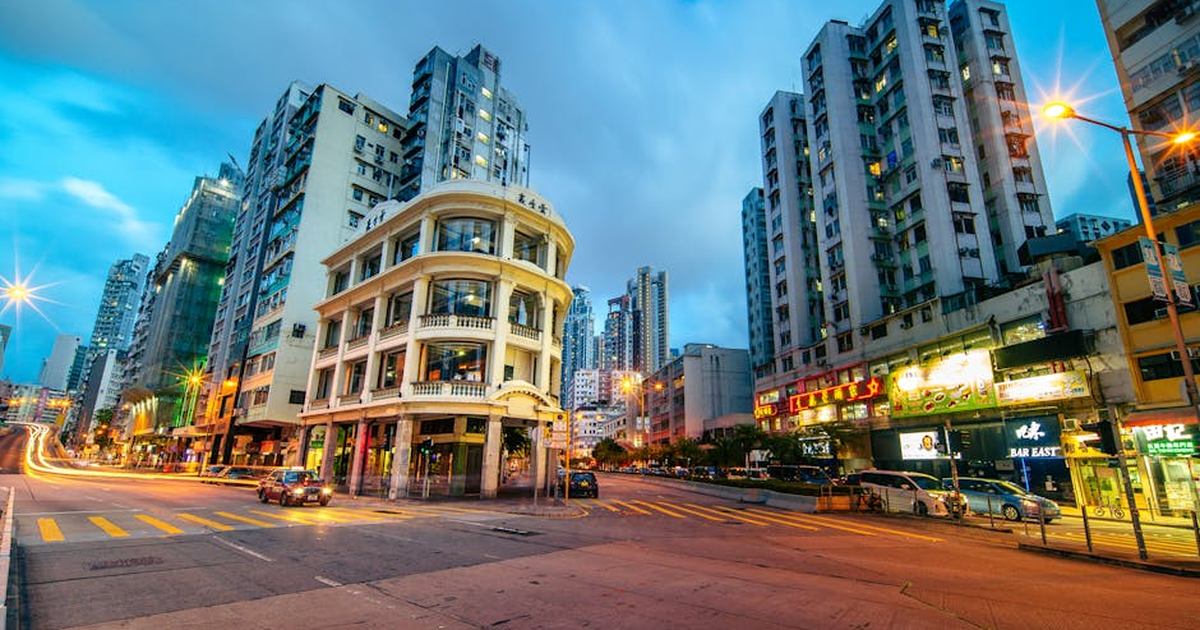 A vibrant street scene featuring a historic building in Kowloon, Hong Kong, during evening twilight.