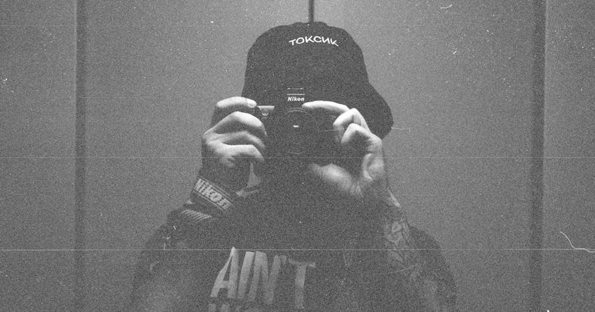 Grainy black and white image of photographer taking a self-portrait in reflection.