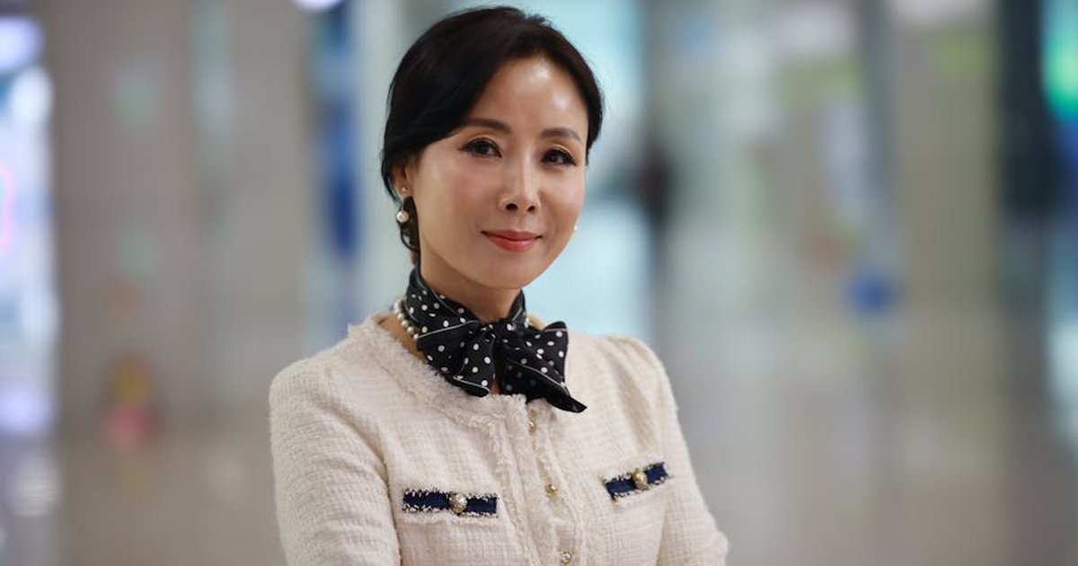 A sophisticated woman smiles confidently in a stylish outfit indoors, exuding elegance and charm.