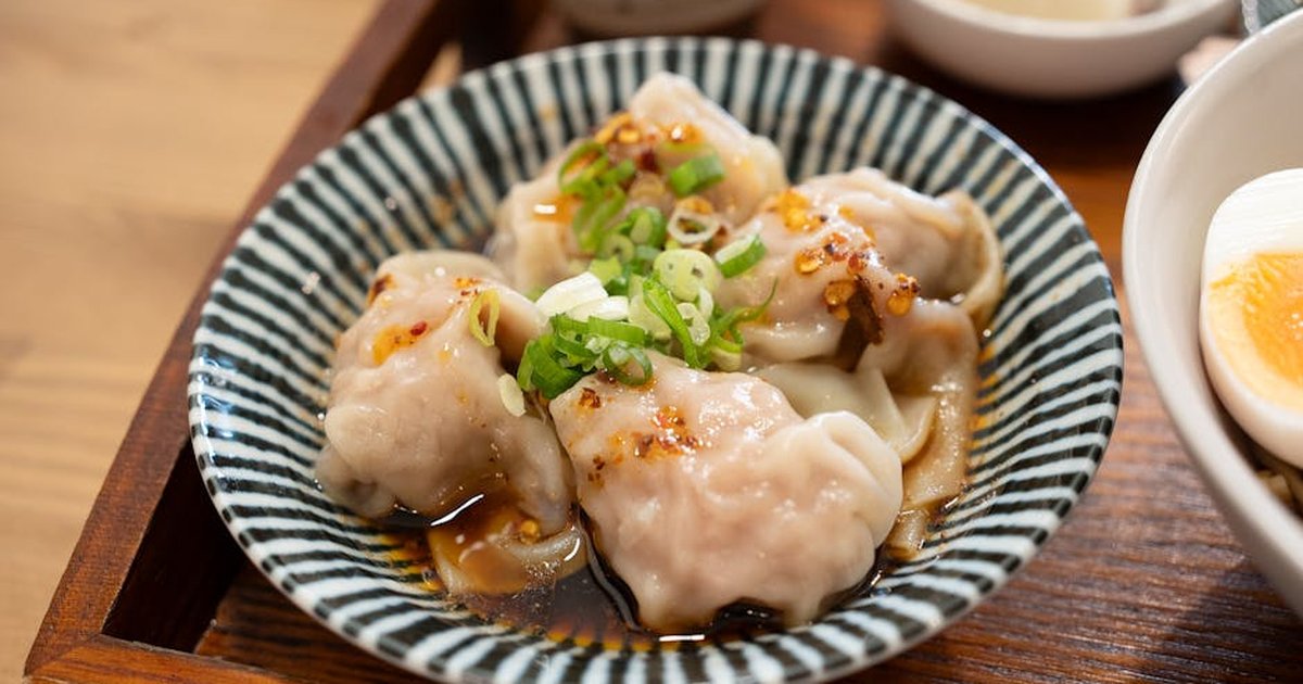 Close-up of savory dumplings with soy sauce, scallions, and chili oil, served on a striped ceramic plate.