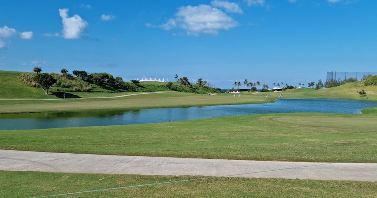 Serene view of a lush green golf course under a bright blue sky with picturesque clouds.
