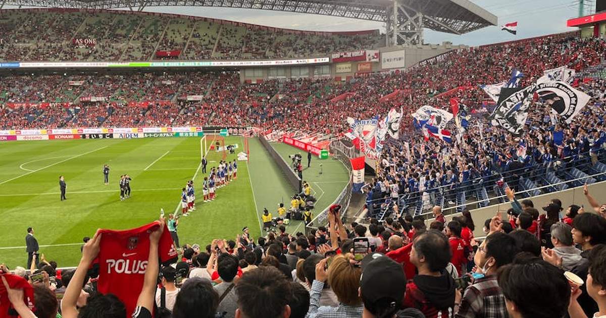 A thrilling soccer match at a packed stadium with energetic fans waving flags and cheering in Japan.