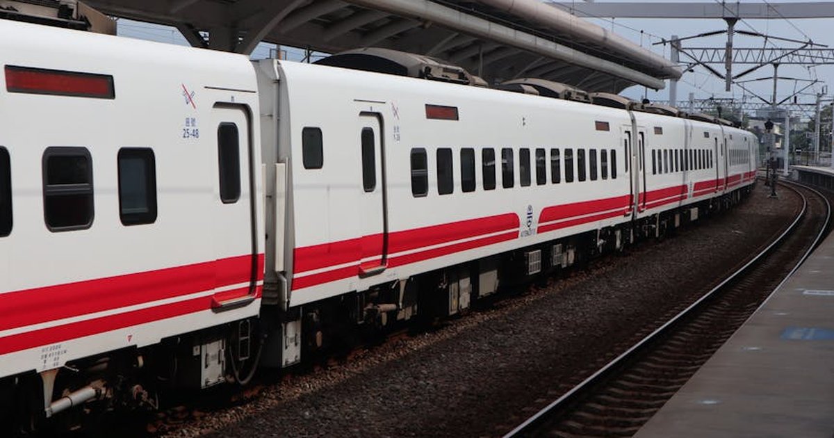 White and red train positioned at an empty railway station platform.