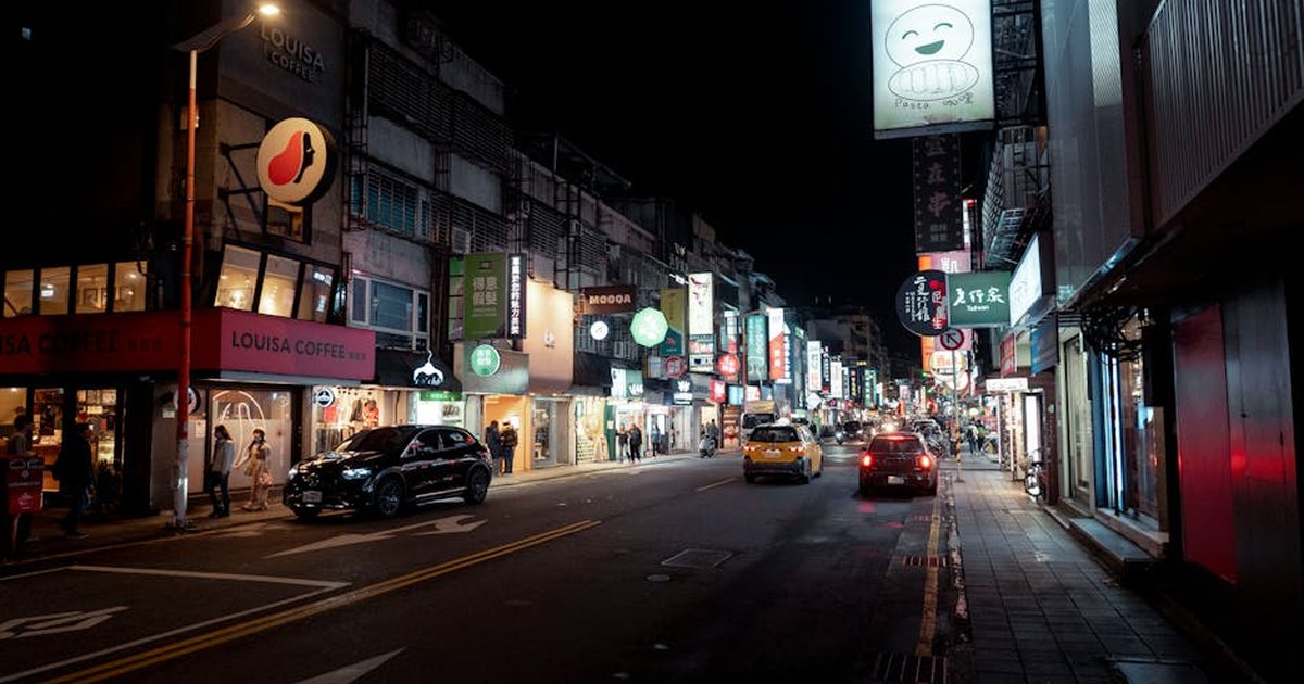 Bustling night street in Taipei with bright city lights and urban activity.